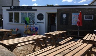 Y tu allan i'r caffi gyda byrddau yn yr awyr agored.