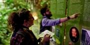 A male pointing at an exhibition board and a female writing on a wipe-clean board in a green jungle environment