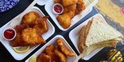Llun o amrywiaeth o bysgod wedi'u ffrio ac opsiynau brechdanau sydd ar gael i'w prynu o Gower Seafood Hut mewn cynwysyddion cludfwyd.