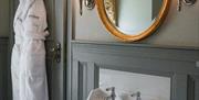 An elegant mirror and lamps above a washbasin in the bathroom. A hotel bath robe hangs on the back of the door.