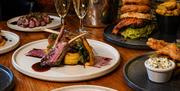 Selection of food on a table. Rack of Gower lamb, beef burger and triple cooked chips and blow torched gurnard fillet.