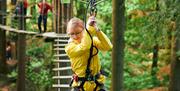Menyw mewn cot law felen yn dringo ar draws rhwystr yn Go Ape Margam