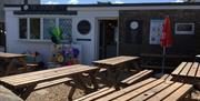 Y tu allan i'r caffi gyda byrddau yn yr awyr agored.